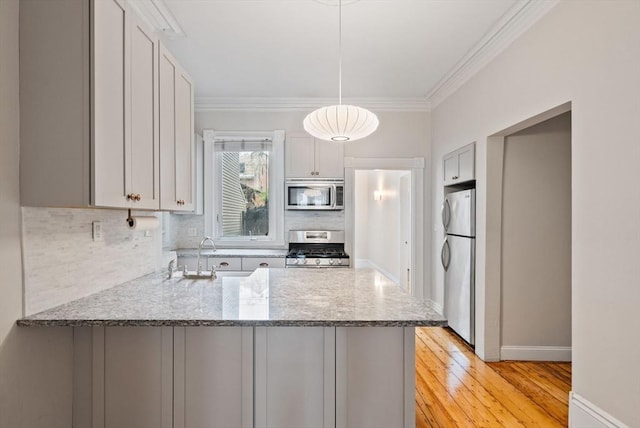 kitchen featuring appliances with stainless steel finishes, a peninsula, decorative backsplash, ornamental molding, and a sink
