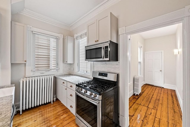 kitchen with appliances with stainless steel finishes, radiator, light countertops, white cabinets, and decorative backsplash
