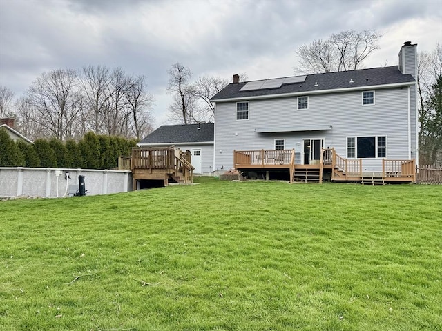 16 E Rd, Adams, MA 01220 - back of house with a wooden deck, roof mounted solar panels, a lawn, and a chimney