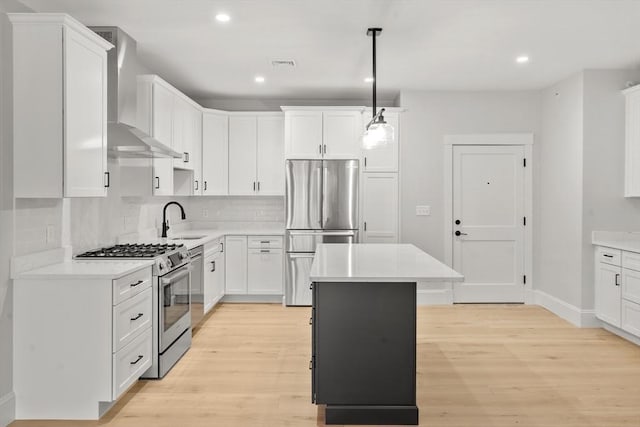 kitchen featuring a center island, wall chimney range hood, pendant lighting, stainless steel appliances, and white cabinets