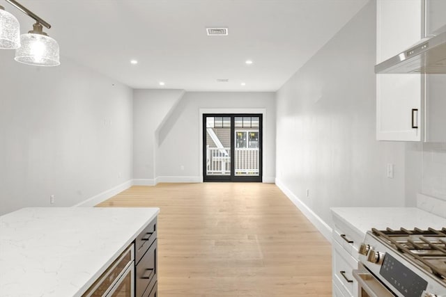 kitchen featuring pendant lighting, light hardwood / wood-style flooring, light stone countertops, white cabinets, and wall chimney exhaust hood