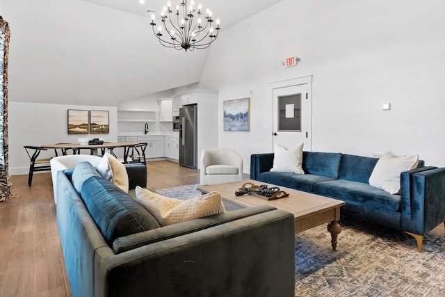 living room with a notable chandelier, high vaulted ceiling, sink, and light wood-type flooring