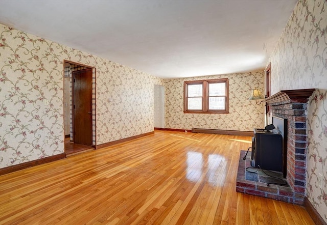 unfurnished living room featuring a brick fireplace, wood finished floors, baseboards, and wallpapered walls