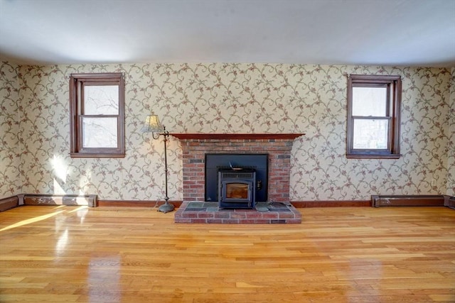 unfurnished living room with baseboards, wood finished floors, a wood stove, and wallpapered walls