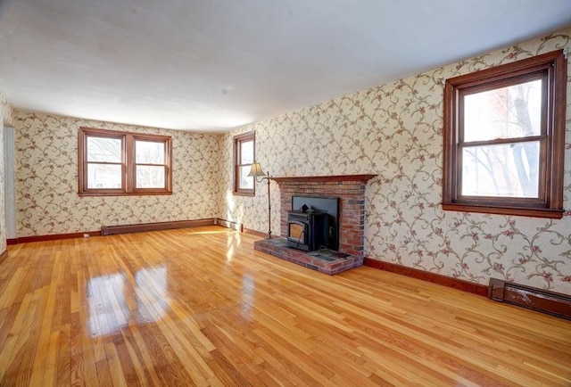 unfurnished living room featuring a wood stove, wallpapered walls, baseboards, and wood finished floors