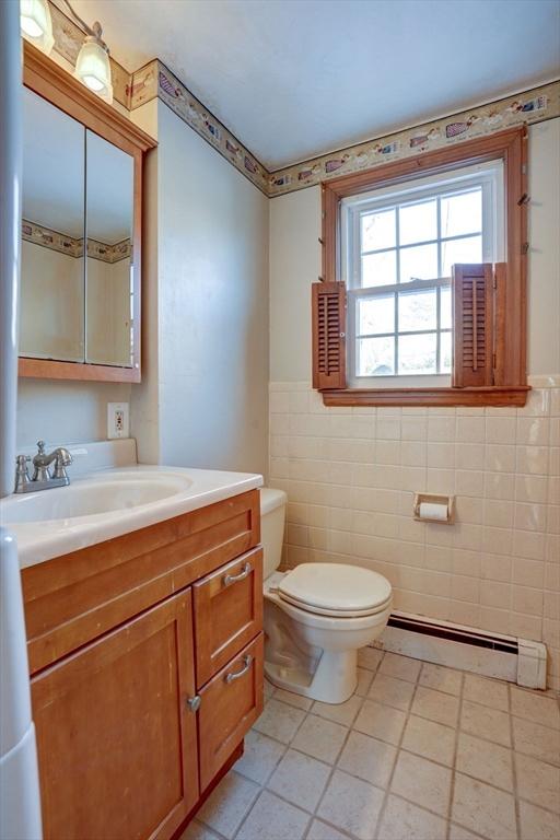 bathroom featuring tile patterned flooring, toilet, vanity, tile walls, and baseboard heating