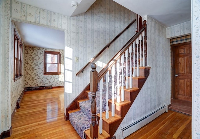 staircase with a baseboard heating unit, wood finished floors, and wallpapered walls