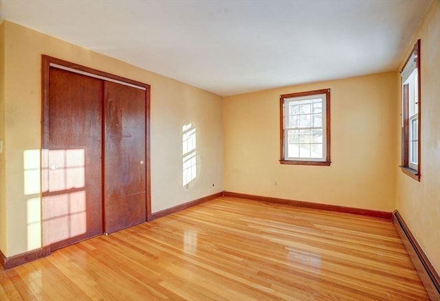 spare room featuring light wood-type flooring, a baseboard radiator, and baseboards