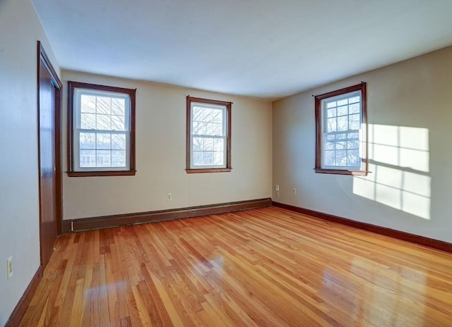 empty room with a baseboard heating unit, light wood finished floors, and baseboards