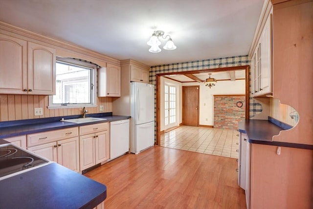 kitchen featuring light wood finished floors, white appliances, dark countertops, and a sink