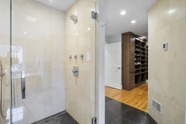 bathroom with a shower with door, hardwood / wood-style flooring, and tile walls