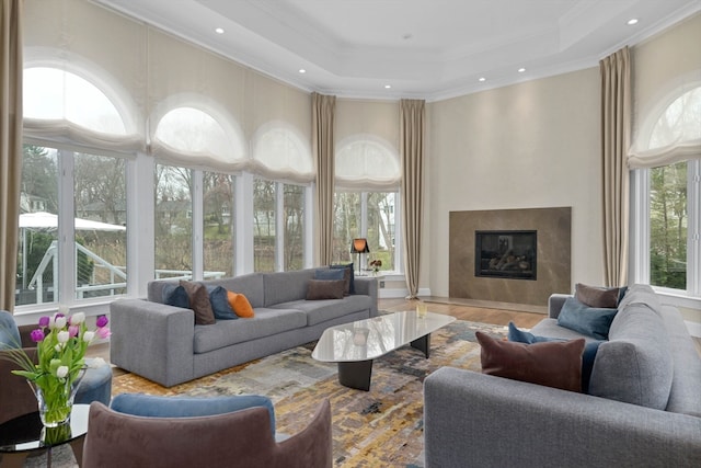 living room featuring crown molding, a raised ceiling, wood-type flooring, and a high end fireplace