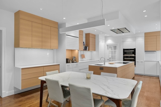 kitchen with light hardwood / wood-style flooring, white cabinets, a kitchen island with sink, and sink