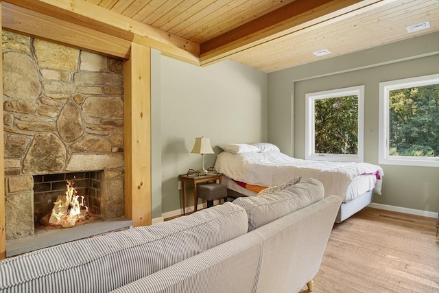 bedroom with light wood-type flooring, beamed ceiling, a fireplace, and wooden ceiling