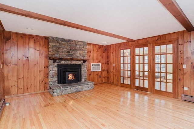 unfurnished living room featuring a stone fireplace, wood walls, an AC wall unit, beamed ceiling, and light hardwood / wood-style floors