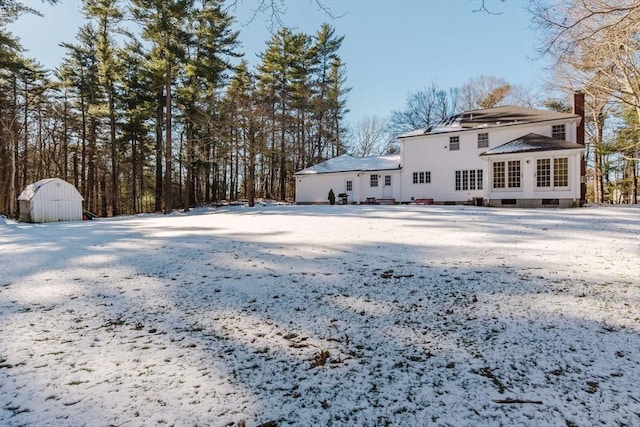 snow covered back of property featuring a shed