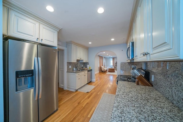 642 Centre St, Newton, MA 02458 - kitchen featuring appliances with stainless steel finishes, arched walkways, a sink, light wood-style flooring, and decorative backsplash