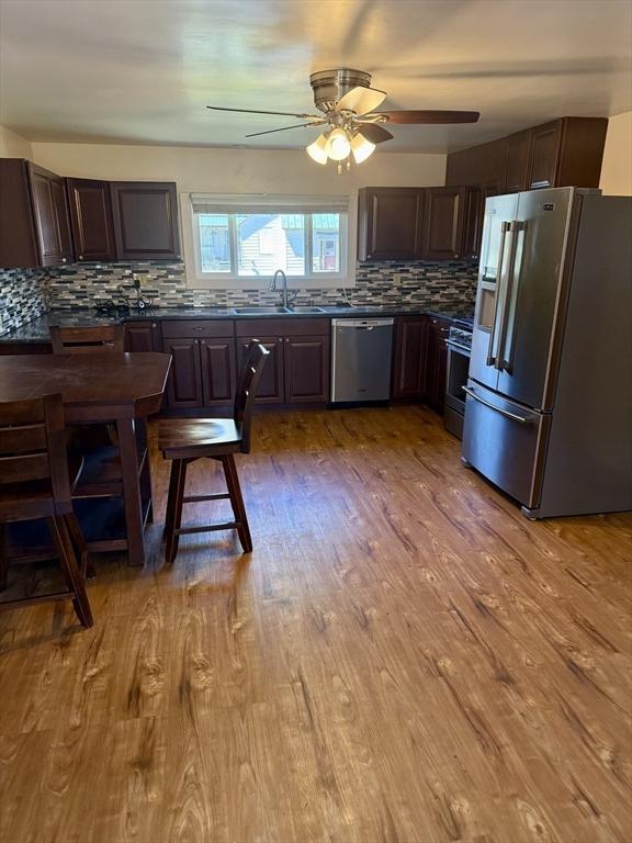 kitchen with dark countertops, appliances with stainless steel finishes, a sink, a ceiling fan, and decorative backsplash