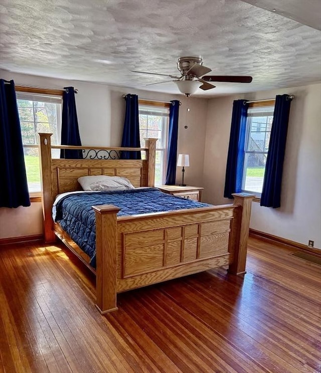 bedroom with baseboards, hardwood / wood-style floors, and multiple windows