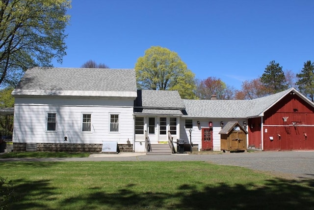 back of property with a chimney, roof with shingles, a lawn, an outbuilding, and entry steps