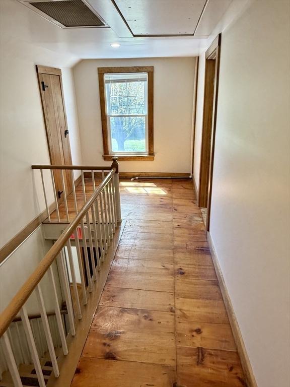 hall with attic access, baseboards, an upstairs landing, light wood-type flooring, and visible vents