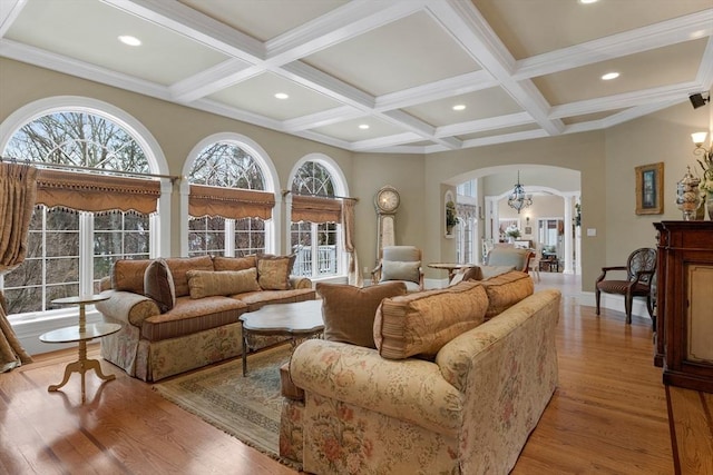 living area with arched walkways, coffered ceiling, light wood-type flooring, beamed ceiling, and an inviting chandelier