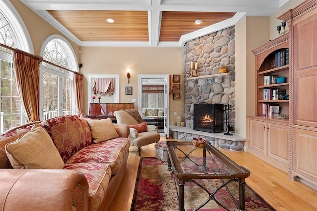 living area featuring beam ceiling, ornamental molding, a stone fireplace, wood finished floors, and wooden ceiling