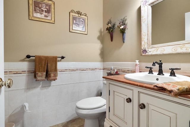 half bathroom featuring toilet, wainscoting, tile walls, and vanity