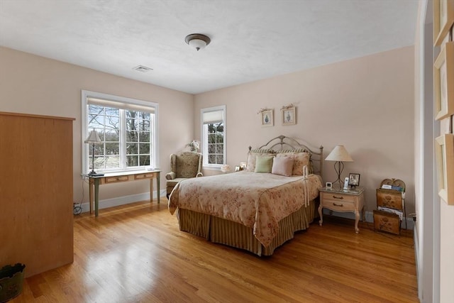 bedroom with light wood finished floors, visible vents, and baseboards