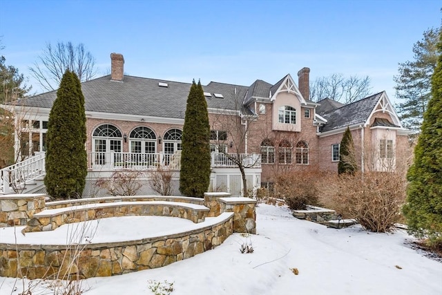 snow covered rear of property with stairway, brick siding, and a chimney