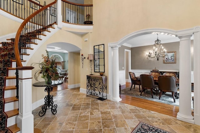 foyer entrance featuring a high ceiling, ornate columns, and an inviting chandelier