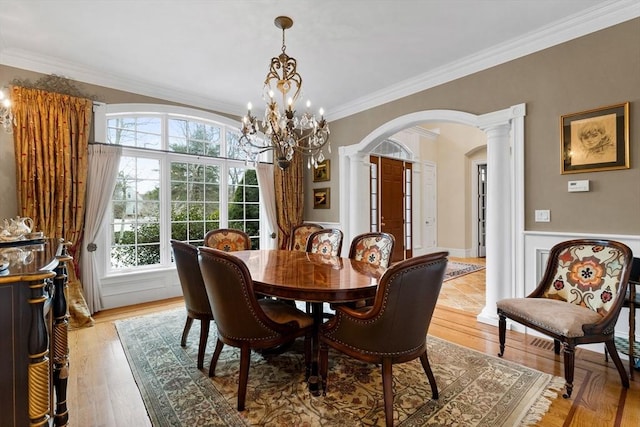 dining area featuring wainscoting, decorative columns, arched walkways, and ornamental molding