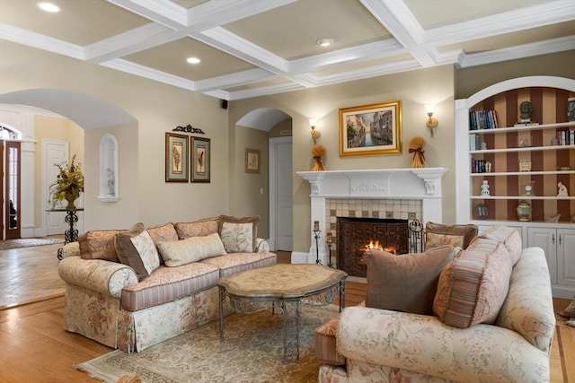 living room with coffered ceiling, a tile fireplace, beamed ceiling, light wood-type flooring, and built in shelves