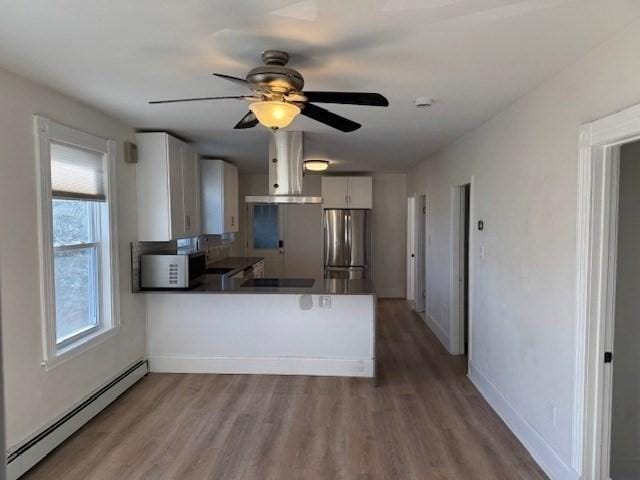 kitchen featuring white cabinets, stainless steel fridge, baseboard heating, kitchen peninsula, and extractor fan