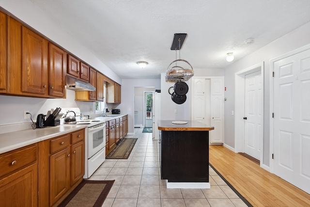 kitchen with light hardwood / wood-style flooring, pendant lighting, white electric range, a center island, and sink