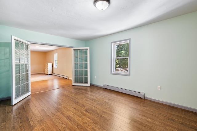 empty room with a wealth of natural light, baseboard heating, and dark hardwood / wood-style floors