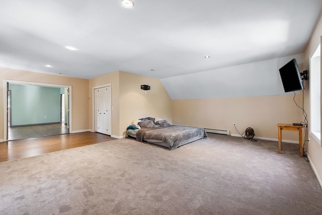 unfurnished bedroom with vaulted ceiling, hardwood / wood-style floors, a baseboard radiator, and a closet