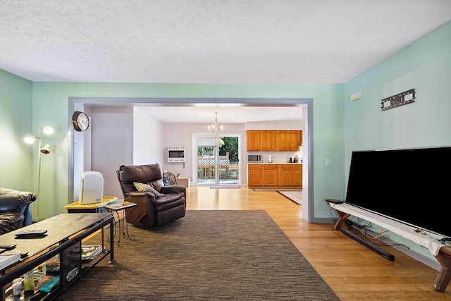 living room with light wood-type flooring, an inviting chandelier, and a textured ceiling