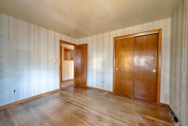 unfurnished bedroom featuring baseboards, wallpapered walls, wood finished floors, and a closet