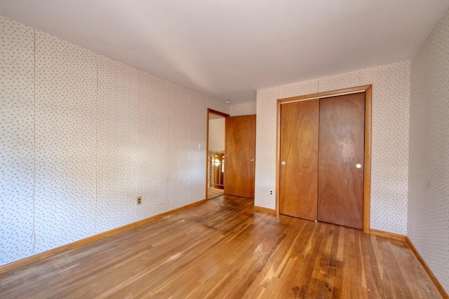 unfurnished bedroom featuring a closet, baseboards, hardwood / wood-style floors, and wallpapered walls