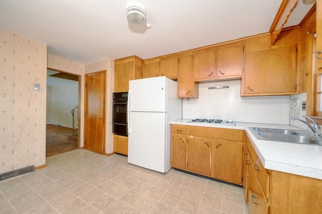 kitchen featuring gas stovetop, a sink, light countertops, freestanding refrigerator, and oven