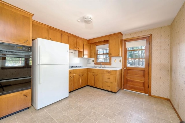 kitchen featuring freestanding refrigerator, oven, wallpapered walls, light countertops, and a warming drawer
