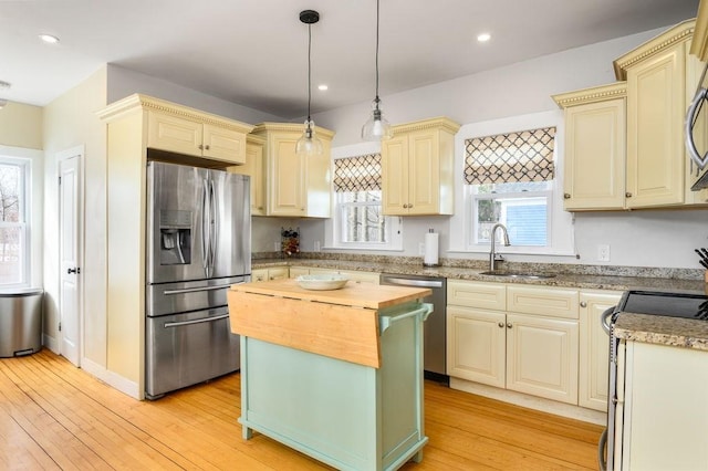 kitchen with stainless steel appliances, butcher block countertops, a sink, cream cabinetry, and light wood finished floors