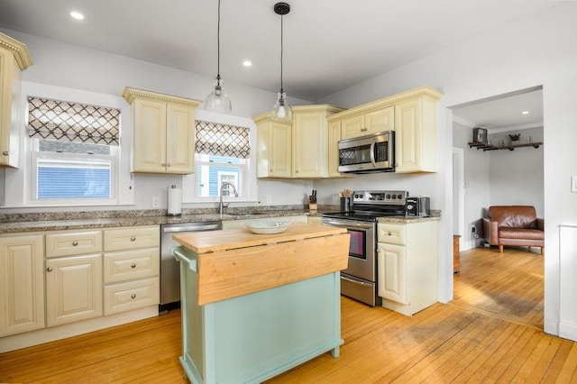 kitchen featuring appliances with stainless steel finishes, wood counters, cream cabinetry, and light wood-style floors