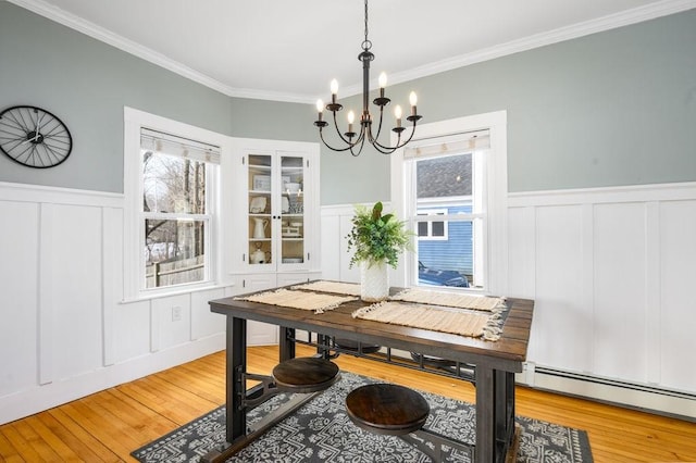 dining room featuring light wood finished floors, a wainscoted wall, an inviting chandelier, crown molding, and a baseboard heating unit