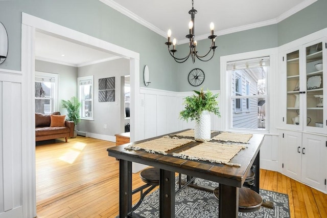 dining space featuring a notable chandelier, ornamental molding, a wainscoted wall, and light wood-style floors