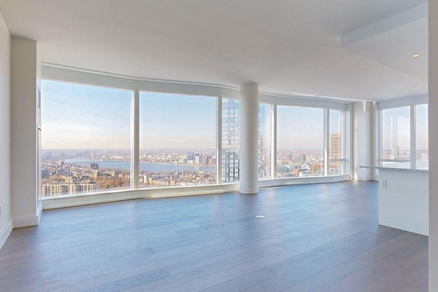 empty room featuring wood finished floors, a view of city, expansive windows, and a water view
