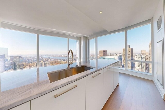 kitchen with a sink, a view of city, white cabinetry, and light stone counters