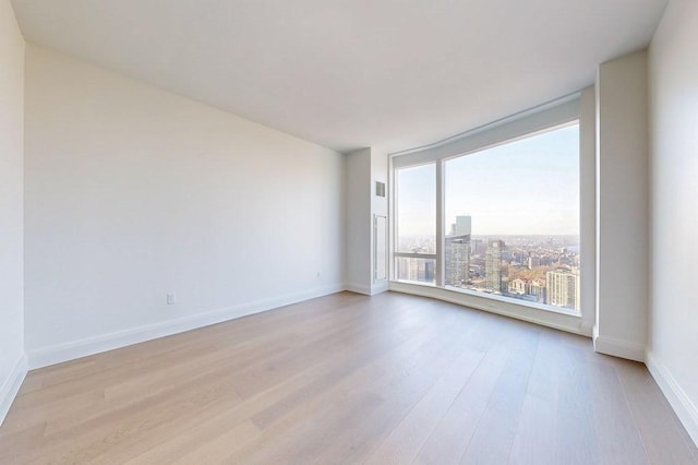 spare room featuring light wood finished floors, baseboards, and a view of city