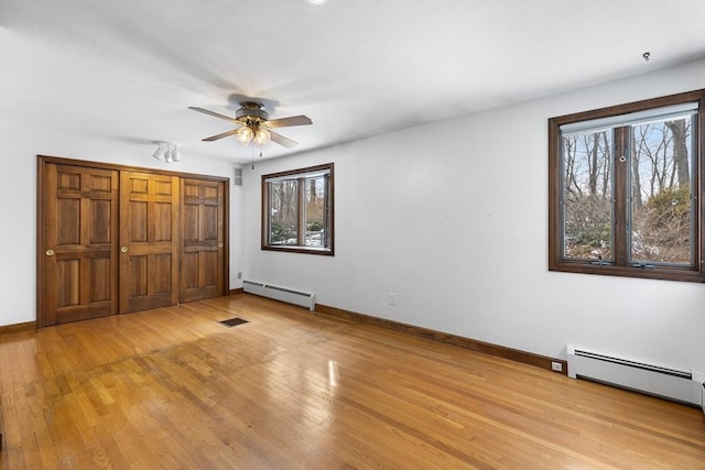 unfurnished bedroom with multiple windows, light wood-type flooring, and baseboard heating